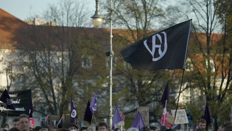 Bandera-De-Anarquía-Negra-Ondeando-Sobre-La-Multitud-De-Berlín-Que-Protesta-Por-La-Situación-De-Inflación-Económica,-Cámara-Lenta