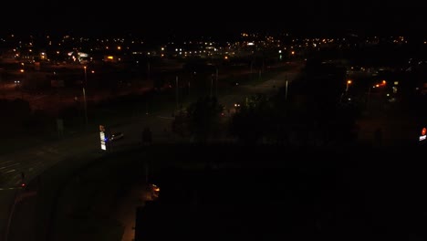 Aerial-view-over-illuminated-McDonalds-fast-food-drive-through-at-night-flying-over-Northern-UK-town-and-highway