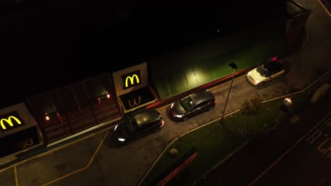 Autos-Estacionados-Esperando-En-La-Comida-Rápida-De-Mcdonalds-En-Coche-Por-La-Noche-Vista-Aérea-En-Aumento