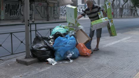 Hombre-Apilando-Cartón-En-Un-Montón-De-Basura-En-Una-Calle-De-Atenas