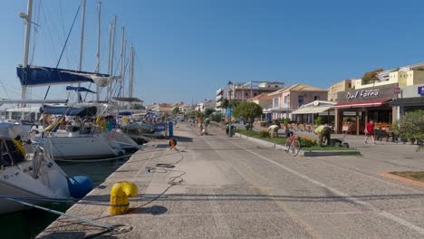 Gente-En-El-Paseo-Marítimo-Con-Yates-Amarrados-Y-Crudos-De-Restaurantes-Y-Cafés,-Preveza,-Grecia