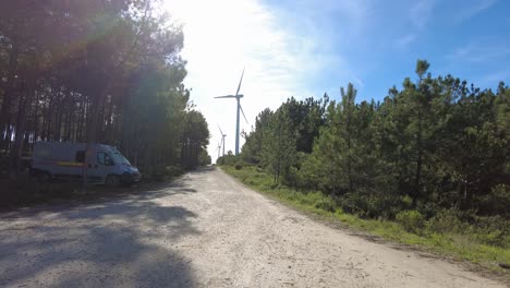 Campervan-hidden-under-pine-trees-with-wind-turbine-spinning-in-the-distance,-Nazare,-Portugal