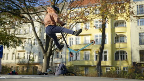 Niño-Pequeño-Intenta-Truco-De-Látigo-De-Cola-En-Un-Scooter-En-El-Parque-De-Patinaje-Local,-Tiro-De-Seguimiento