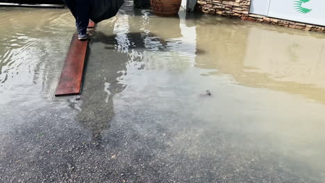 Menschen-Treten-Auf-Eine-Holzplattform,-Um-Zu-Vermeiden,-Dass-Wasser-Auf-Die-Straße-Kommt