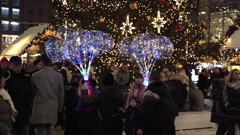 People-with-LED-balloons-and-crowd-below-Christmas-tree,-night-Prague