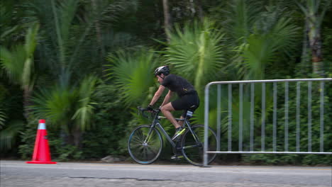 Zeitlupe-Eines-Männlichen-Athleten,-Der-Einen-Schwarzen-Anzug-Und-Einen-Helm-Trägt,-Der-Sein-Fahrrad-Auf-Der-Radsportbühne-Eines-Triathlons-Fährt