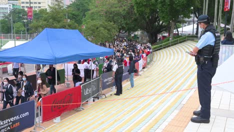 A-police-officer-stands-guard-as-spectators-and-rugby-enthusiasts-queue-in-line-to-enter-the-stadium-holding-the-Hong-Kong-Seven-rugby-tournament,-one-of-the-city's-highest-profile-sport-events