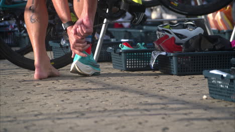 Cierre-En-Cámara-Lenta-De-Un-Atleta-Masculino-Que-Finaliza-La-Etapa-De-Ciclismo-En-Un-Triatlón-Preparándose-Para-La-Etapa-De-Carrera-Poniéndose-Sus-Zapatos-Para-Correr