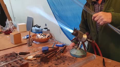 Close-up-of-a-glassblower-artisan-shaping-the-hot-molten-glass-at-strong-fire-inside-a-workshop