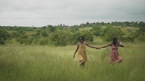 Two-carefree-young-attractive-Asian-females-holding-hands-while-walking-through-a-grass-field-on-a-beautiful-day-outdoors,-India