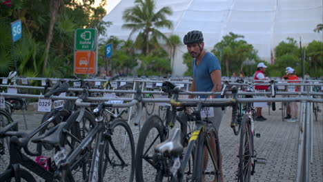 Atleta-Latino-Masculino-Con-Casco-Preparando-Su-Bicicleta-En-El-Punto-De-Transición-La-Tarde-Antes-De-La-Competencia-De-Triatlón