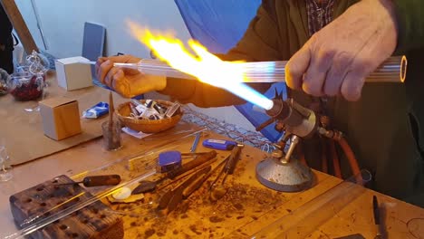 Close-up-of-a-glassblower-artisan-shaping-the-hot-molten-glass-at-strong-fire-inside-a-workshop