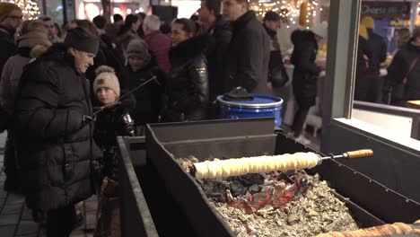 Lady-Rastrillando-Las-Brasas-De-La-Parrilla-Debajo-De-La-Torta-De-La-Chimenea,-Mercado-Navideño-De-Praga