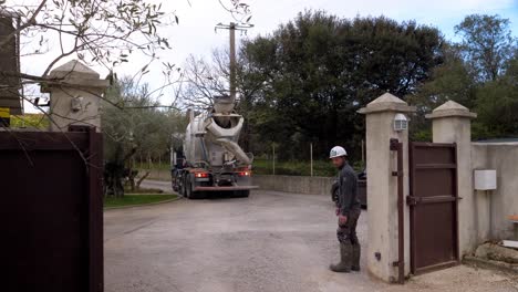 Trabajador-De-La-Construcción-Tratando-De-Ayudar-Al-Conductor-A-Estacionar-El-Camión-De-Cemento-A-Través-De-La-Puerta