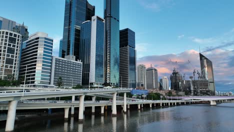 Drone-shot-above-river-panning-up-showing-Brisbane-CBD,-Expressway-Motorway-along-river,-Casino,-with-Skyscraper-'The-One'-centred