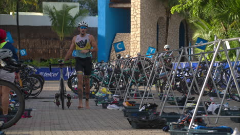 Cámara-Lenta-De-Un-Atleta-Masculino-Corriendo-A-Lo-Largo-De-Su-Bicicleta-Descalzo-Terminando-La-Etapa-De-Ciclismo-Entrando-En-La-Zona-De-Transición-En-Un-Triatlón