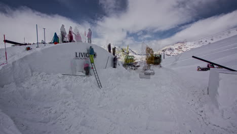 Shot-of-workers-building-igloo-with-white-snow-covered-by-a-yellow-colored-crane-in-Livigno,-Italy-on-a-cold-winter-day-in-timelapse