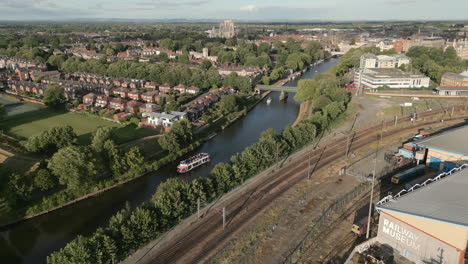 Pullback-Drohne-Aus-Der-Luft,-Die-Das-Nationale-Eisenbahnmuseum-Mit-Der-Kathedrale-Von-York-Minster-Und-Dem-Fluss-Ouse-Mit-Touristenfähre-Im-Hintergrund-An-Einem-Sonnigen-Abend-In-North-Yorkshire,-Großbritannien,-Enthüllt