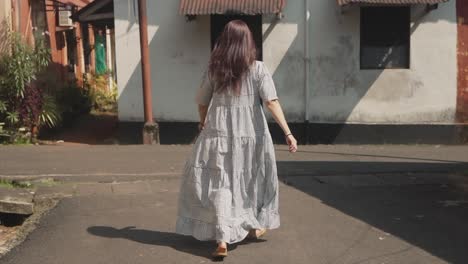 Brunette-Indian-woman-walking-in-front-of-the-camera,-in-the-historical-streets-of-Fontainhas,-India,-on-a-sunny-day