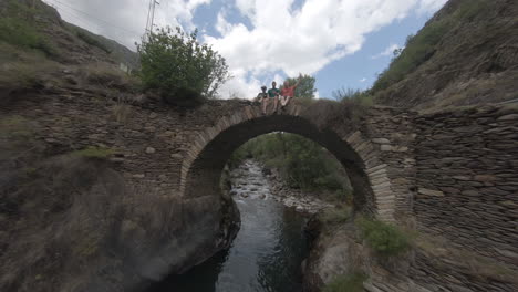 Drone-Aéreo-Fpv-Deportivo-Volando-Sobre-El-Arroyo-Del-Río-Hacia-El-Puente-Con-La-Gente