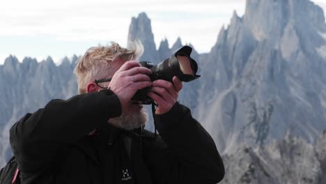 Hiker-Man-rotating-Dial-in-Camera-whilst-Taking-Pictures-on-Top-of-Mountain