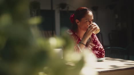 Beautiful-Indian-woman-drinking-coffee,-sitting-outside-in-the-morning,-with-a-dreamy-and-happy-look,-in-Fontainhas,-India