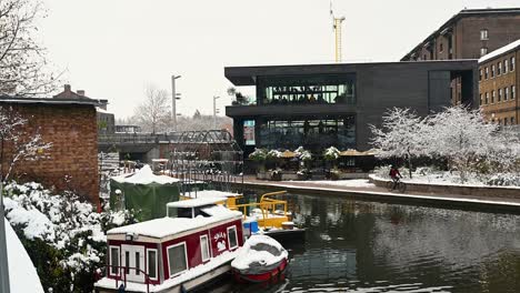 Cycling-past-the-Swan-boat-on-a-snowy-morning,-Kings-Cross,-St-Pancreas,-London,-United-Kingdom