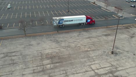 pleasing-aerial-of-a-red-semi-truck-driving-in-a-big-empty-parking-lot-autumn