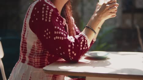 Beautiful-Indian-woman-drinking-her-morning-coffee-while-sitting-outside,-wearing-a-red-summer-dress,-in-Fontainhas,-India