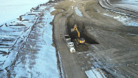 Ein-Bagger-Kippt-Schmutz-In-Einen-Wartenden-Schwertransporter-Bei-Einem-Neubauprojekt-Westlich-Von-Calgary,-Alberta,-Kanada