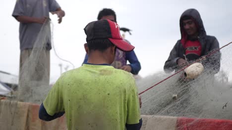 Vista-De-La-Parte-Posterior-Del-Pescador-Local-Clasificando-La-Red-De-Pesca-Con-Trabajadores-En-Gwadar