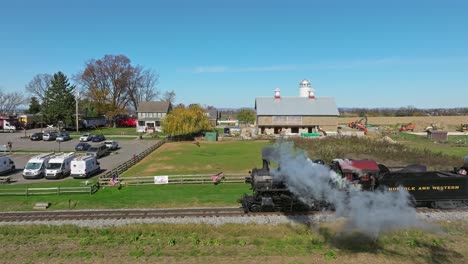 An-Aerial-Ahead-and-Parallel-View-of-a-Single-Rail-Road-Track-With-a-Steam-Train-Blowing-Smoke-on-a-Sunny-Fall-Day