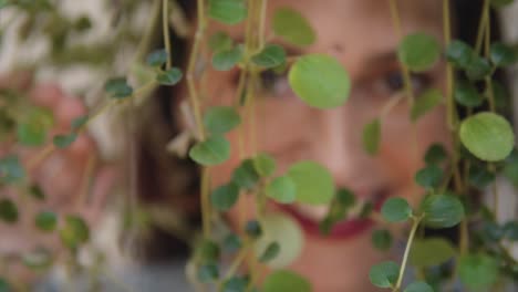 Portrait-of-a-Indian-woman-with-a-beautiful-smile,-hiding-behind-some-leaves,-out-of-focus,-in-Fontainhas,-India