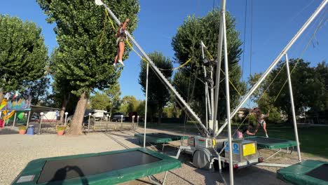 Excited-little-kid-girls-trying-to-back-flip-while-bouncing-on-trampoline-with-harness