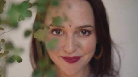 Portrait-of-a-beautiful-Indian-woman-with-a-bright-smile,-hiding-behind-some-leaves,-out-of-focus,-in-Fontainhas,-India