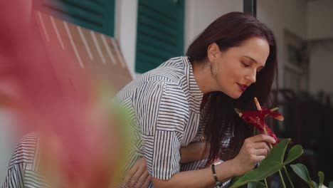 Beautiful-Indian-woman-smelling-red-flowers-with-a-soft-smile,-wearing-a-summer-dress,-in-the-town-of-Fontainhas,-India