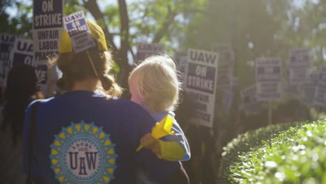 A-Young-Woman-Holding-a-Baby-Marches-on-the-Picket-Line-with-UC-Academic-Workers-Holding-Signs-in-the-Background-at-UCLA