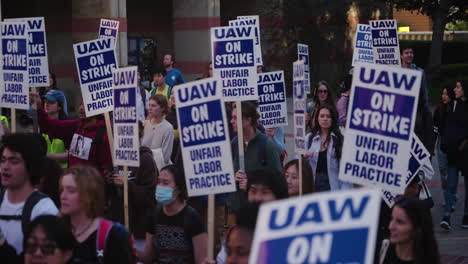 Una-Panorámica-En-Cámara-Lenta-De-Una-Gran-Multitud-De-Trabajadores-Académicos-Con-Carteles-Marchando-En-El-Campus-De-Ucla