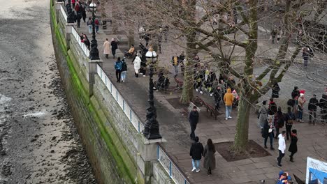 People-walking-past-the-National-Theatre-while-the-tide-is-low-on-the-Thames,-London,-United-Kingdom