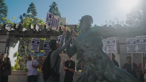 Eine-Junge-Akademikerin-Hält-Einer-Statue-Auf-Dem-Campus-Der-Ucla-Ein-Streikzeichen-Der-Uaw-In-Die-Hände