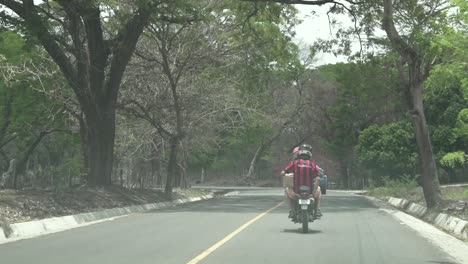 Zwei-Männer,-Die-Mit-Helmen-Auf-Einem-Motorrad-Entlang-Einer-Einspurigen-Straße-Fahren,-Hinterher-Geschossen