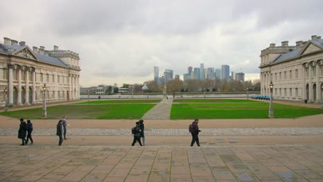 Estudiantes-Caminando-En-El-Antiguo-Colegio-Naval-Real-Con-El-Horizonte-De-Londres-En-El-Fondo-En-Inglaterra,-Reino-Unido