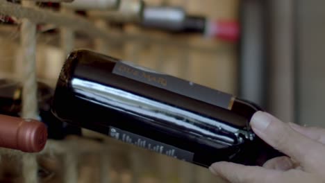 Close-up-of-person-putting-back-a-bottle-of-red-wine-back-on-the-wine-rack