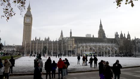 Turistas-En-Los-Jardines-De-La-Plaza-Del-Parlamento-Cubiertos-De-Nieve-En-El-Frío-Día-De-Invierno-En-Diciembre-Con-El-Big-Ben-Y-Las-Casas-Del-Parlamento-En-El-Fondo