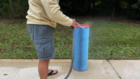 Man-wearing-shorts-and-flip-flops-cleaning-swimming-pool-filter-with-water-hose