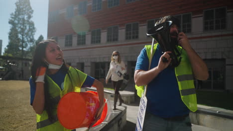 Un-Líder-De-Huelga-De-Hombre-Y-Mujer-Toca-Un-Tambor-Y-Canta-En-Un-Megáfono-En-El-Campus-En-La-Huelga-De-Trabajadores-Académicos-De-Ucla