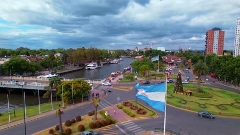 Bandera-Argentina-Ondeando-En-La-Rotonda-Del-Delta-Del-Parana,-Tigre,-Toma-Aérea-De-Drones-Durante-El-Día,-Tráfico-De-Tranvías