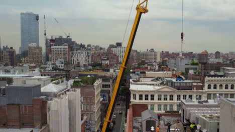 Vista-Aérea-De-La-Grúa-Que-Transporta-La-Carga-Por-Encima-De-Los-Trabajadores-En-La-Raíz-Del-Edificio-Residencial-En-Manhattan,-Nueva-York,-Ee.uu.