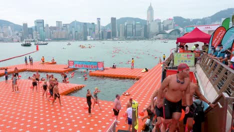 Los-Participantes-Y-Los-Entusiastas-De-La-Natación-Cruzan-La-Línea-De-Meta-Durante-La-Competencia-Anual-De-Natación-New-World-Harbour-Race-Mientras-El-Horizonte-De-Hong-Kong-Se-Ve-En-El-Fondo