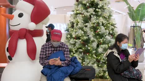 Käufer-Sitzen-Auf-Einer-Bank-Neben-Einem-Weihnachtsbaum-Und-Einer-Schneemanninstallation-In-Einem-Einkaufszentrum-In-Hongkong